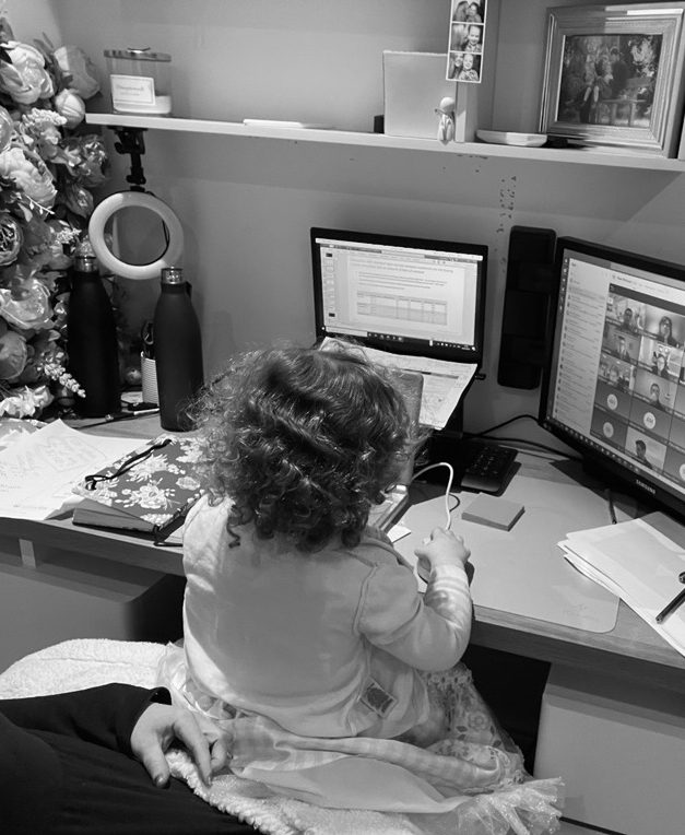 Little girls sitting on parents lap whilst Mum works with her latop. Working Mum reality